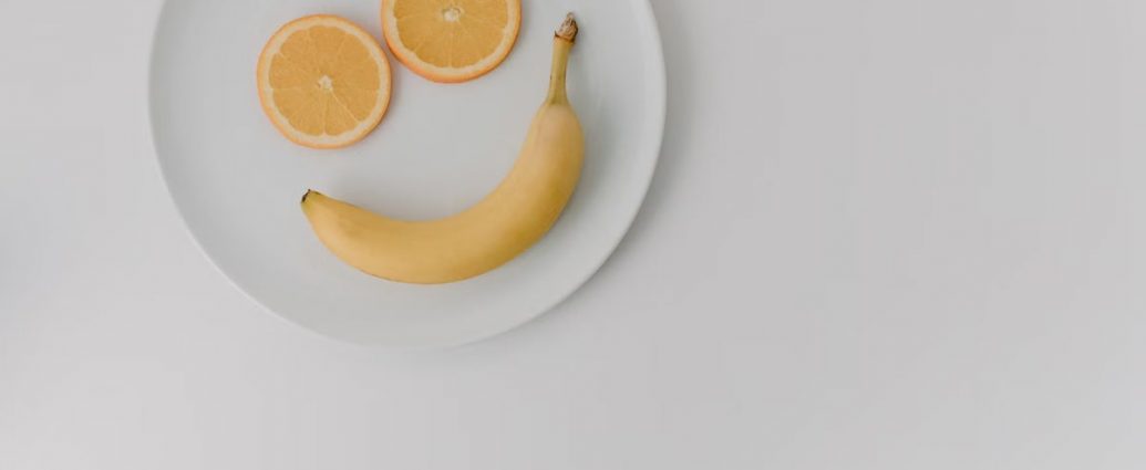 A playful arrangement of banana and orange slices forming a smile on a white plate.