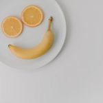 A playful arrangement of banana and orange slices forming a smile on a white plate.