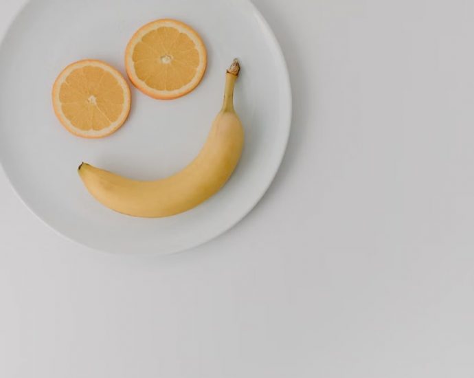 A playful arrangement of banana and orange slices forming a smile on a white plate.